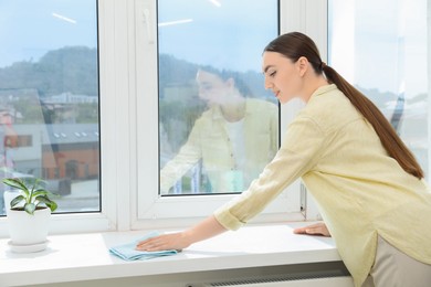 Beautiful young woman cleaning windowsill at home