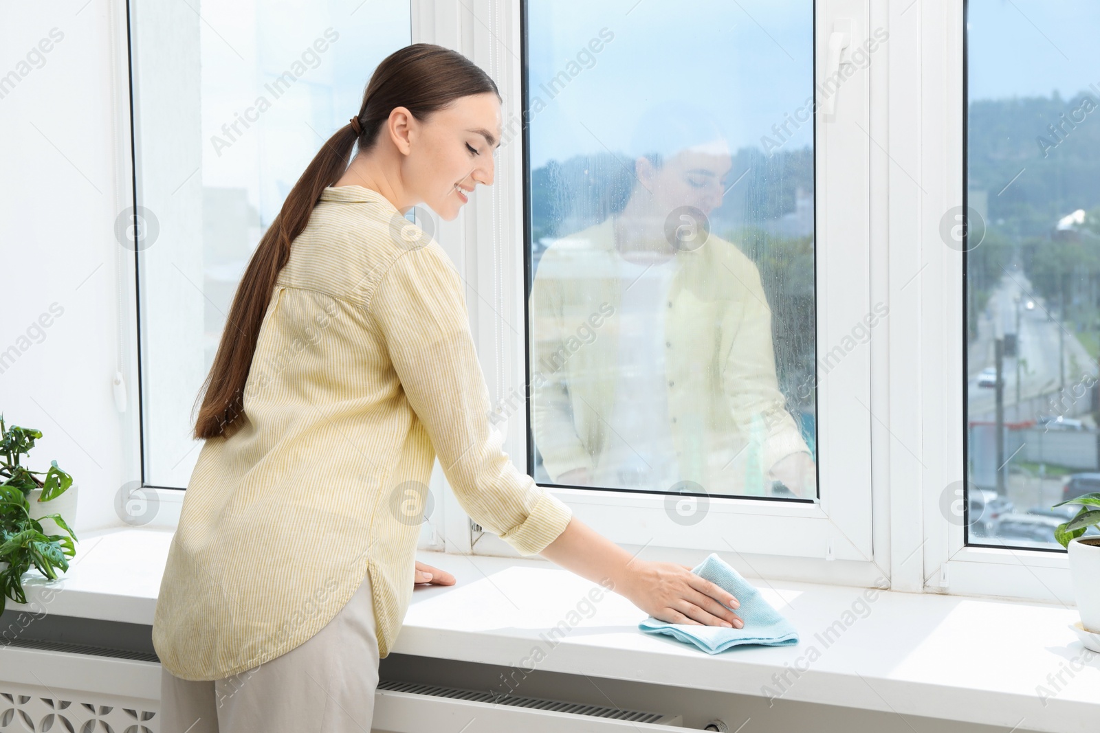 Photo of Beautiful young woman cleaning windowsill at home