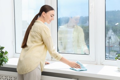 Beautiful young woman cleaning windowsill at home