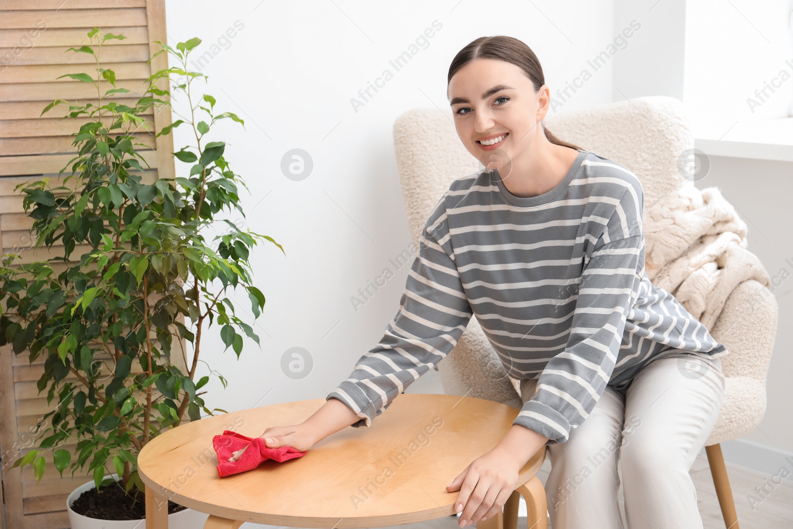 Photo of Beautiful young woman wiping coffee table with rag at home