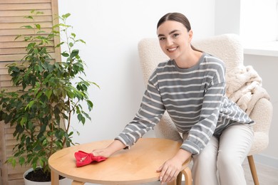 Beautiful young woman wiping coffee table with rag at home