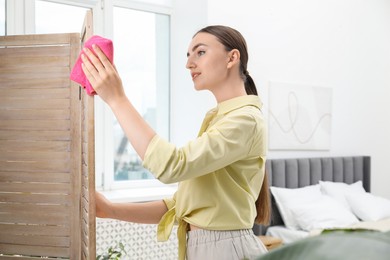 Beautiful young woman wiping folding screen with rag in bedroom