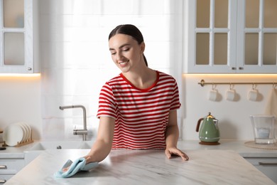 Beautiful young woman wiping white marble table with rag in kitchen