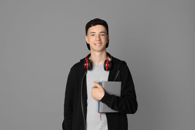 Photo of Portrait of teenage boy with headphones and books on grey background