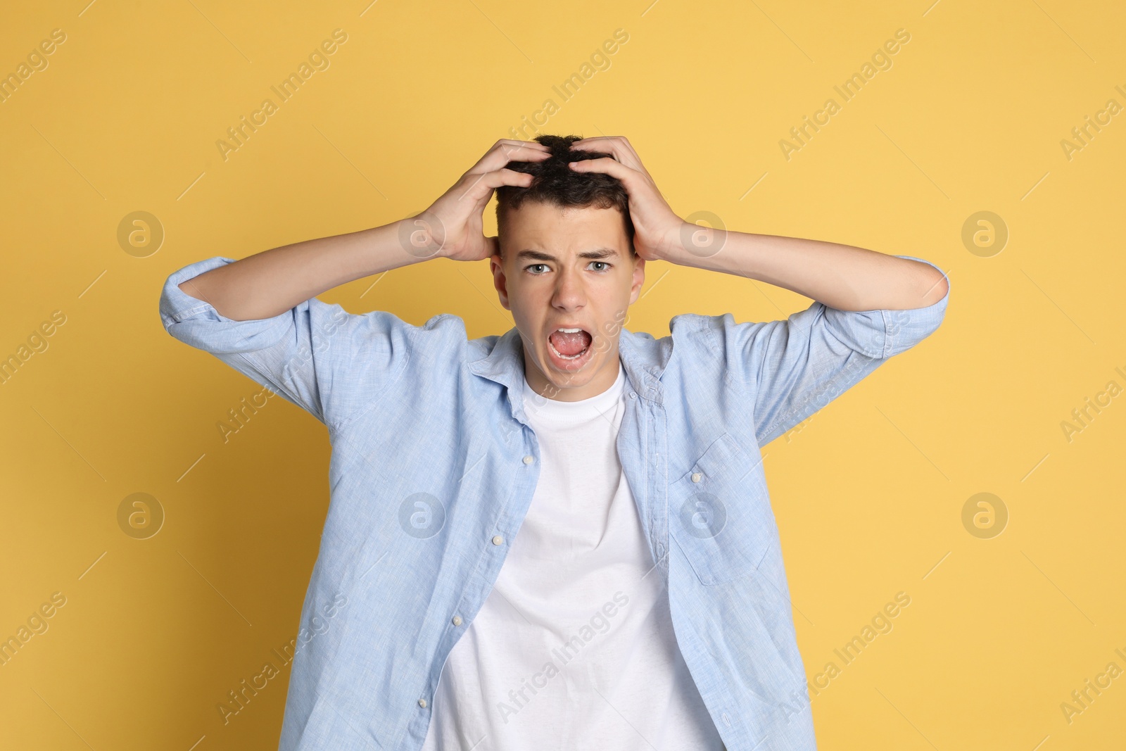 Photo of Portrait of angry teenage boy on yellow background