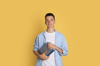 Photo of Portrait of teenage boy with books on yellow background