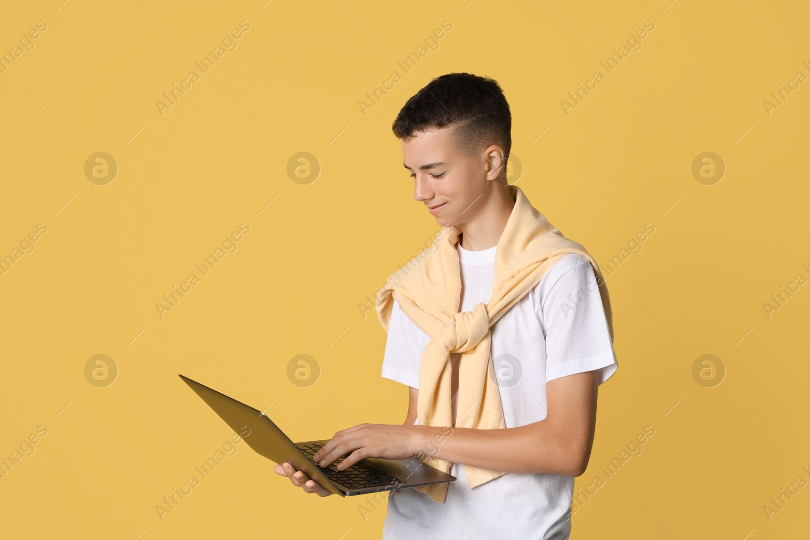 Photo of Portrait of teenage boy with laptop on yellow background