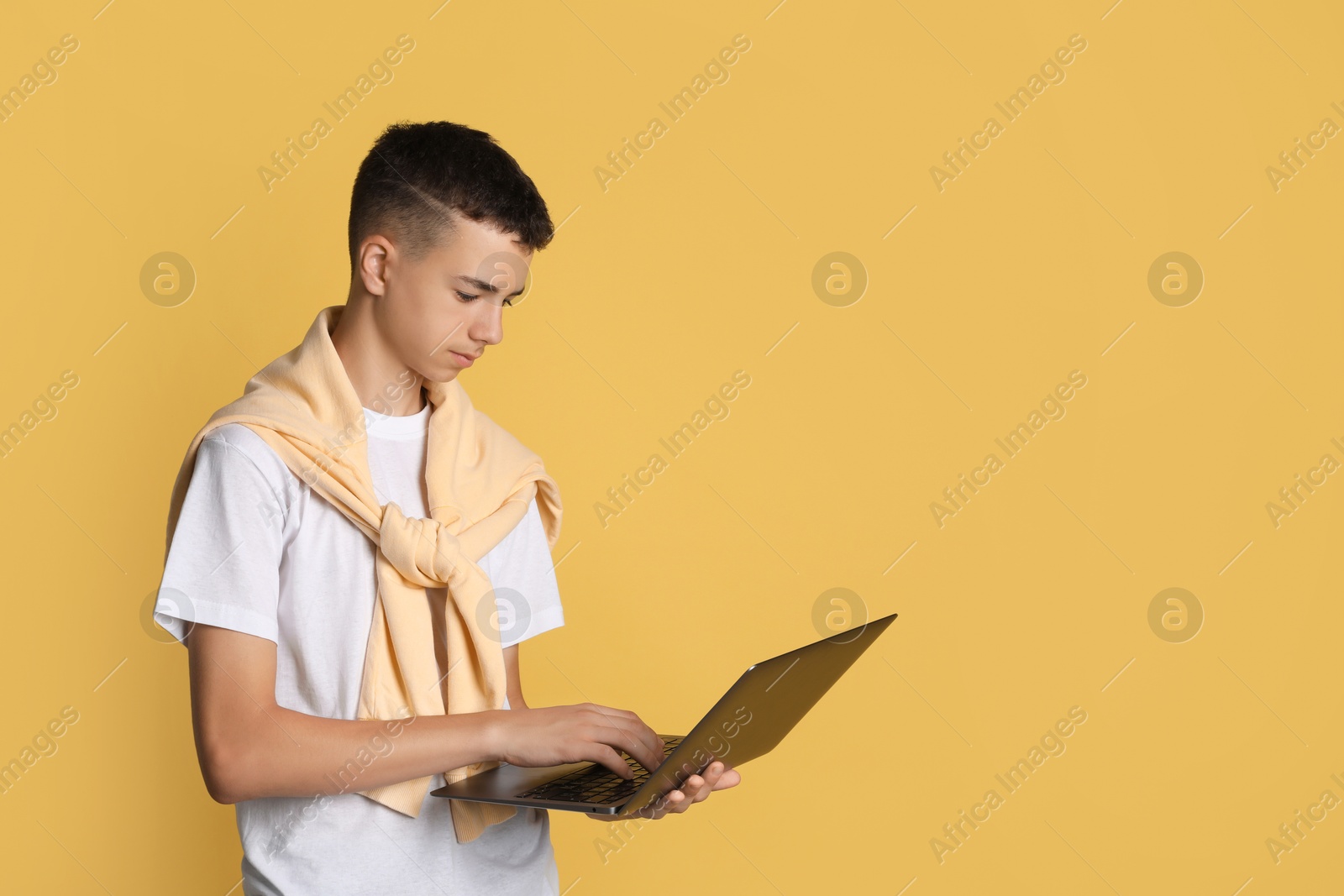 Photo of Portrait of teenage boy with laptop on yellow background, space for text