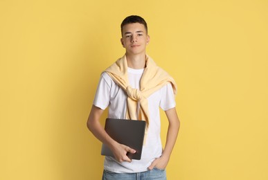 Photo of Portrait of teenage boy with laptop on yellow background