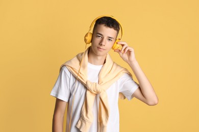 Portrait of teenage boy with headphones on yellow background