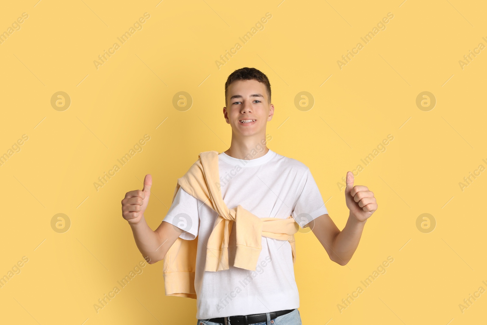 Photo of Portrait of teenage boy showing thumbs up on yellow background