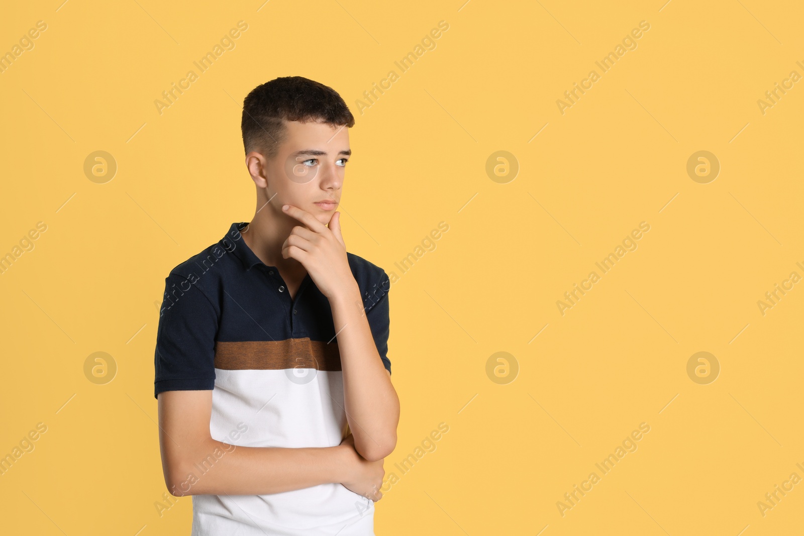 Photo of Portrait of thoughtful teenage boy on yellow background, space for text