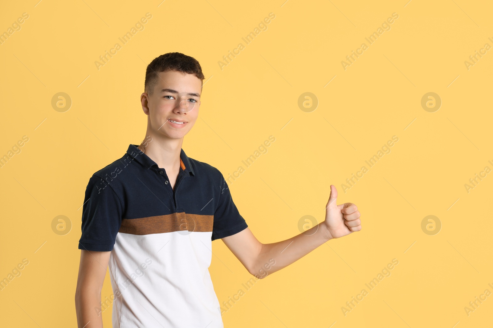 Photo of Portrait of teenage boy showing thumbs up on yellow background. Space for text