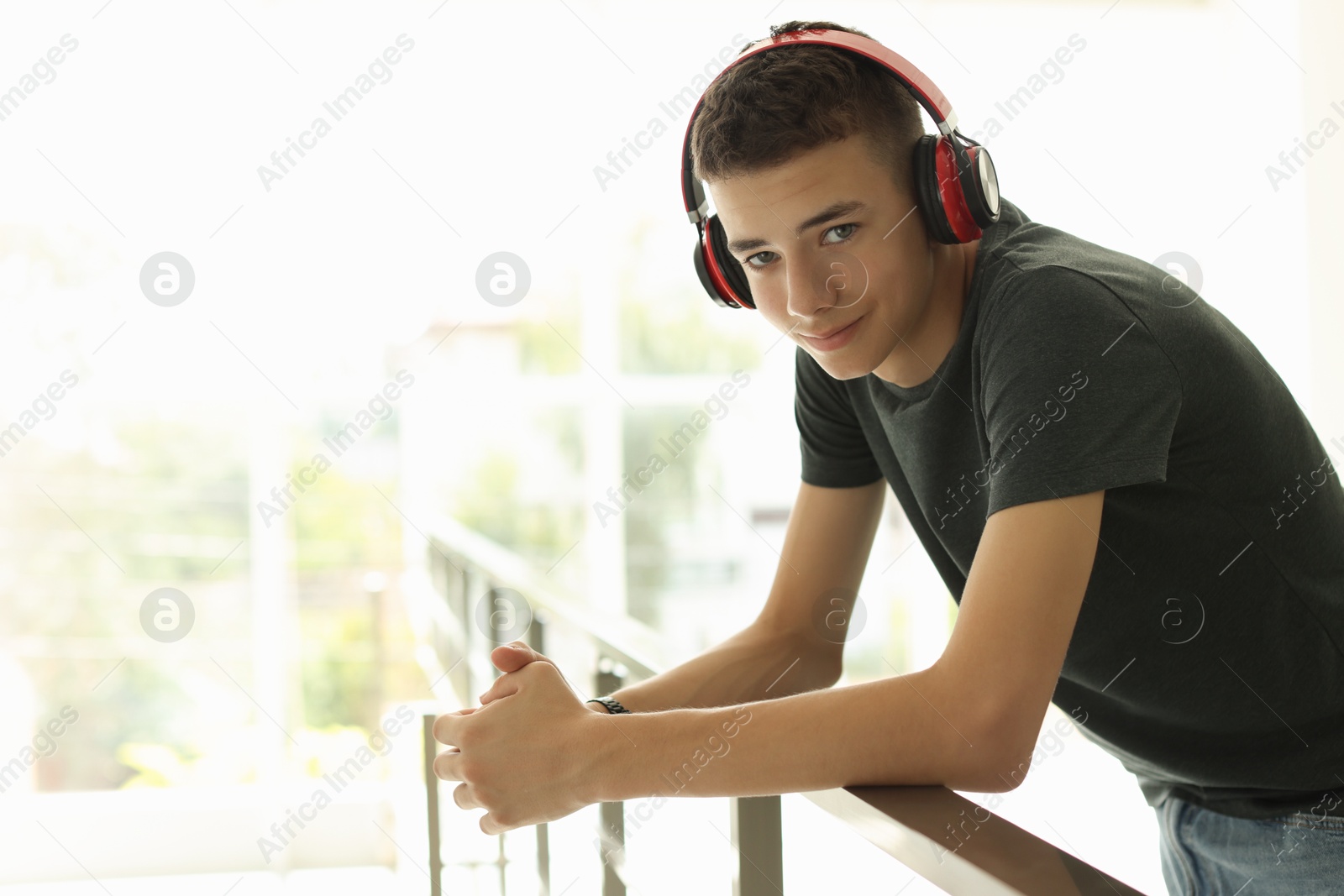 Photo of Portrait of teenage boy listening to music near railings indoors. Space for text