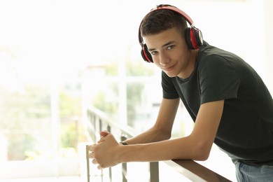 Portrait of teenage boy listening to music near railings indoors. Space for text