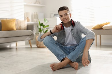 Full length portrait of teenage boy sitting on floor at home. Space for text