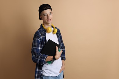 Photo of Portrait of smiling teenage boy with books on dark beige background. Space for text