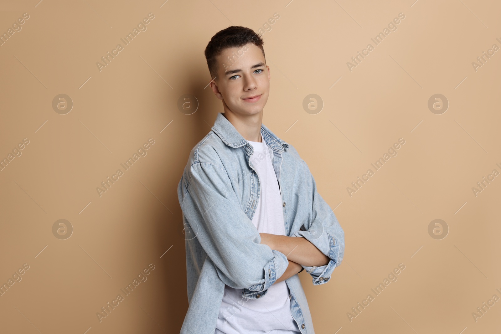 Photo of Portrait of teenage boy with crossed arms on dark beige background