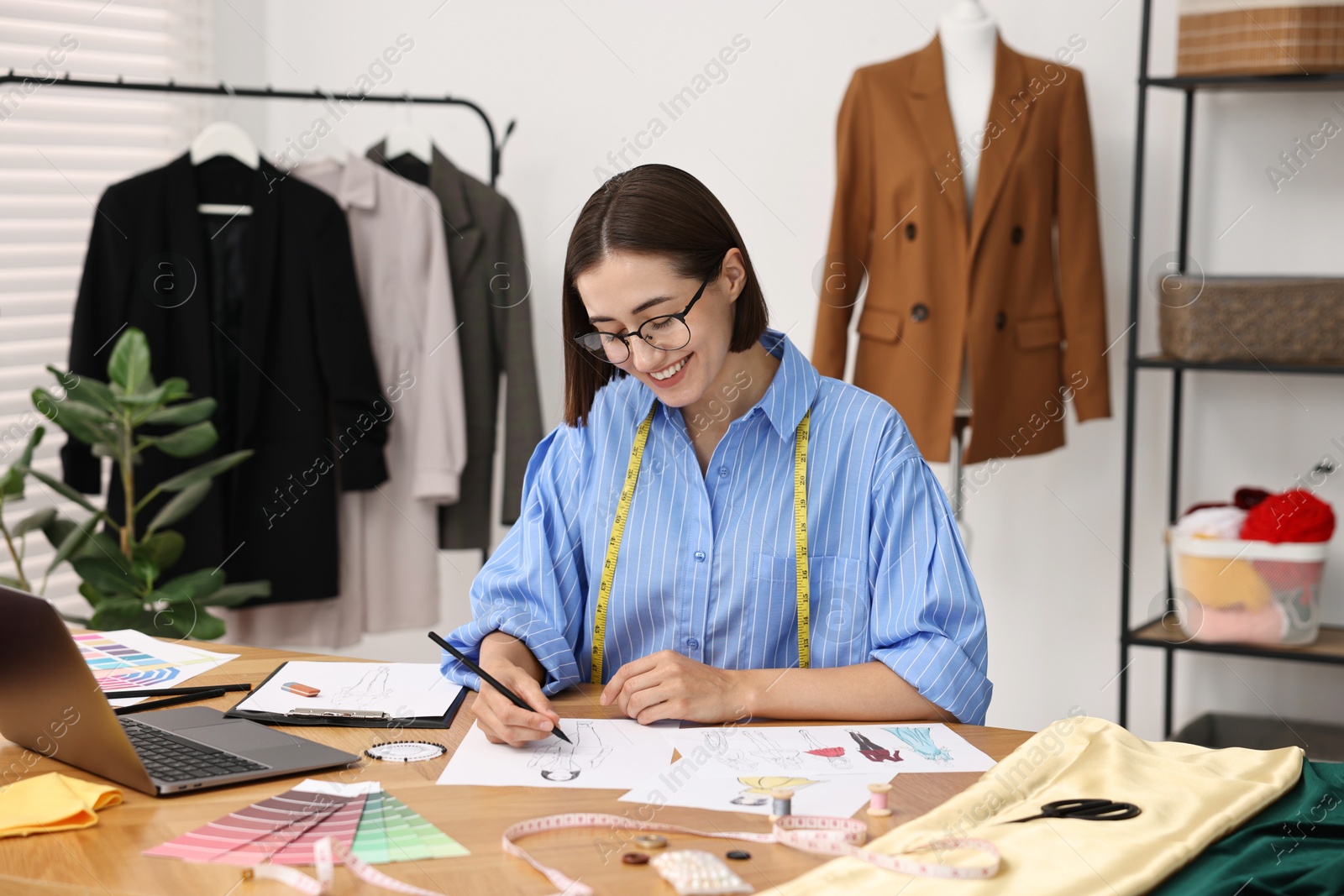 Photo of Fashion designer drawing sketch of beautiful outfit at wooden table in workshop