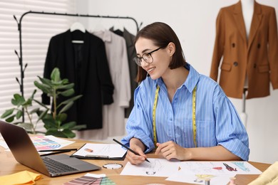 Fashion designer drawing sketch of beautiful outfit at wooden table in workshop