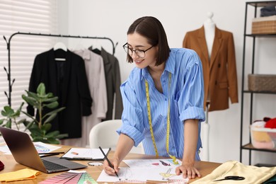 Fashion designer drawing sketch of beautiful outfit at wooden table in workshop