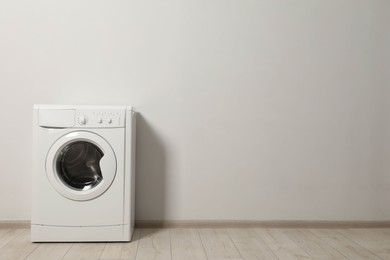 Photo of Washing machine near white wall indoors, space for text