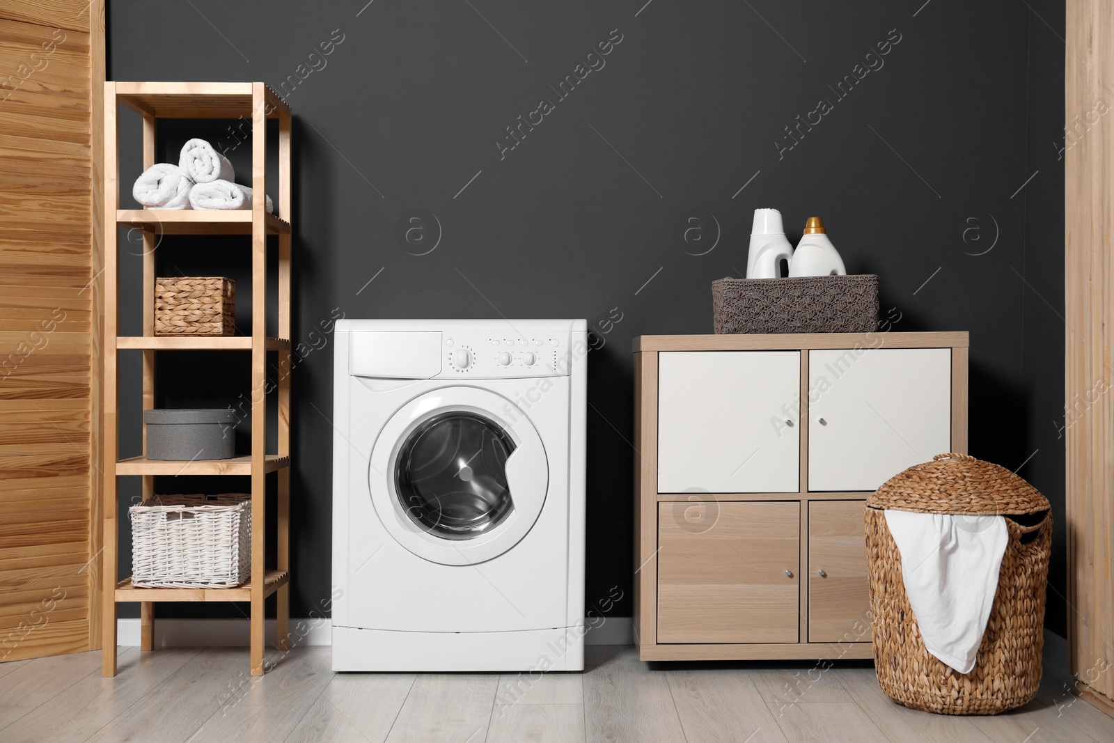 Photo of Washing machine, detergents in basket, wooden rack and storage cabinet indoors