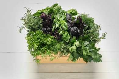 Photo of Different fresh herbs in basket on white wooden table, above view