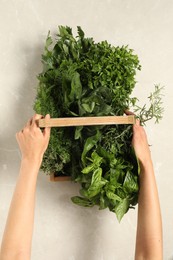 Photo of Woman holding different fresh herbs in wooden basket at light table, top view