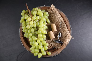 Photo of Corkscrew with metal handle, corks, grapes and wooden barrel on grey table, top view