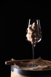 Corkscrew, glass and corks on wooden barrel against black background