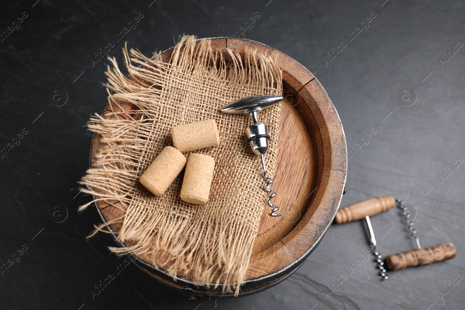 Photo of Different corkscrews, corks and wooden barrel on grey table, above view