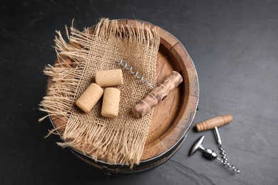 Different corkscrews, corks and wooden barrel on grey table, above view