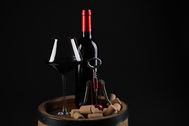 Wing corkscrew, bottle of wine, glass and corks on wooden barrel against black background