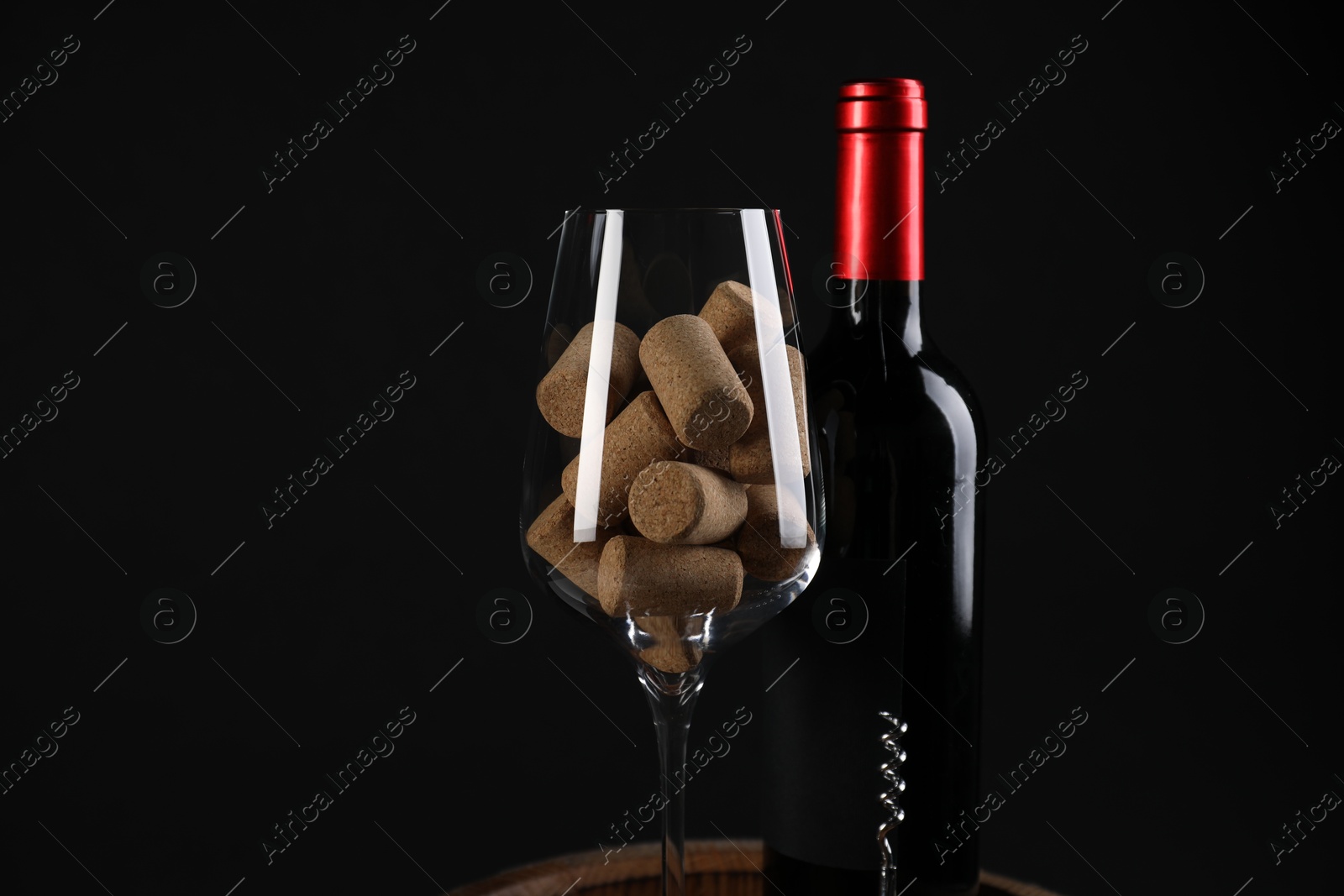 Photo of Corkscrew, bottle of wine, glass and corks against black background