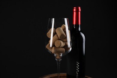 Photo of Corkscrew, bottle of wine, glass and corks against black background