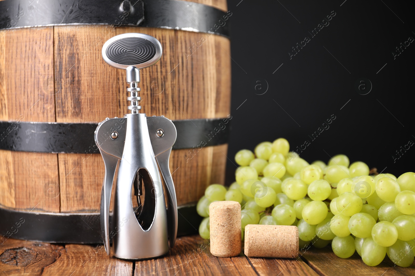 Photo of Wing corkscrew, corks, grapes and barrel on wooden table