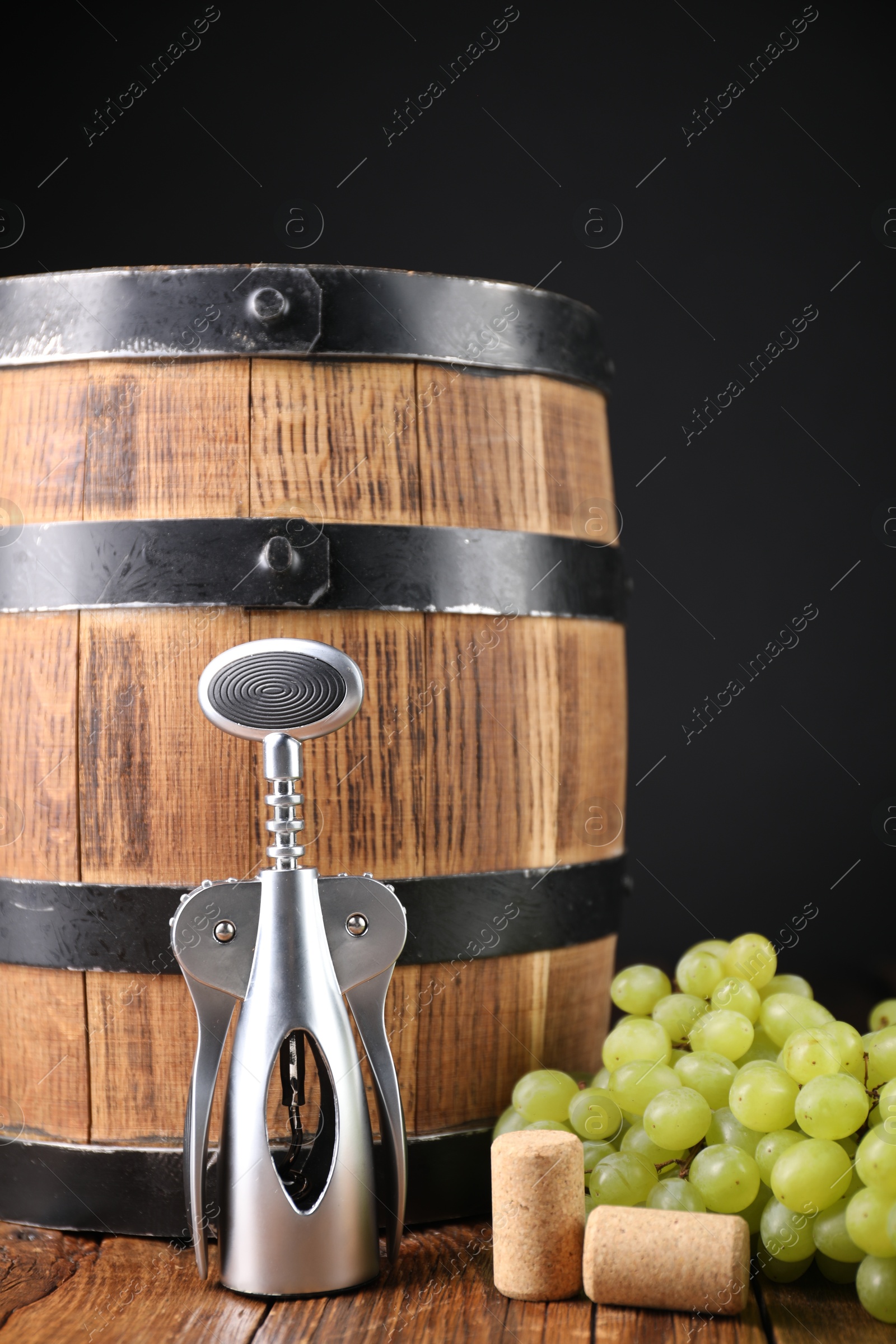 Photo of Wing corkscrew, corks, grapes and barrel on wooden table