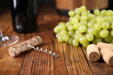 Photo of Corkscrew, corks and grapes on wooden table, closeup