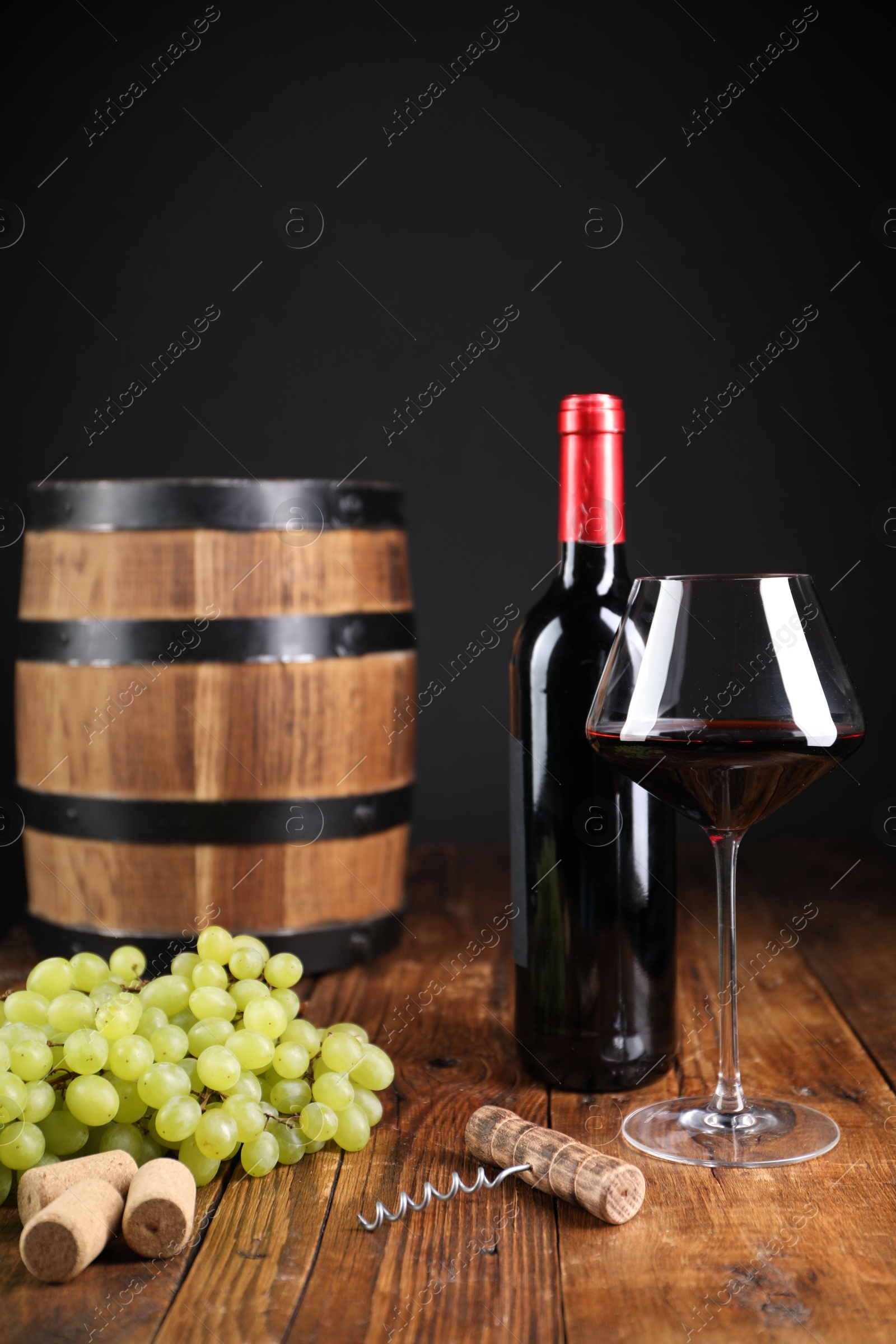 Photo of Corkscrew, corks, bottle of wine, glass, grapes and barrel on wooden table