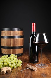 Photo of Corkscrew, corks, bottle of wine, glass, grapes and barrel on wooden table