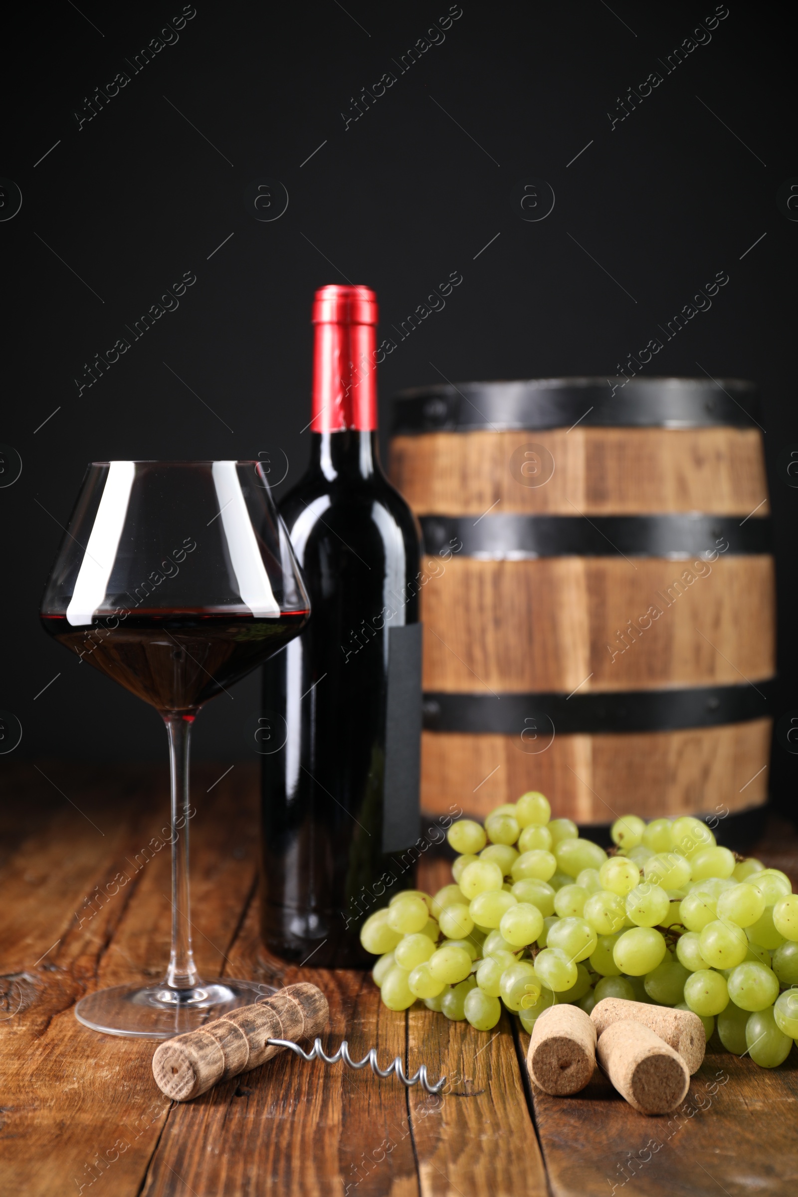 Photo of Corkscrew, corks, bottle of wine, glass, grapes and barrel on wooden table