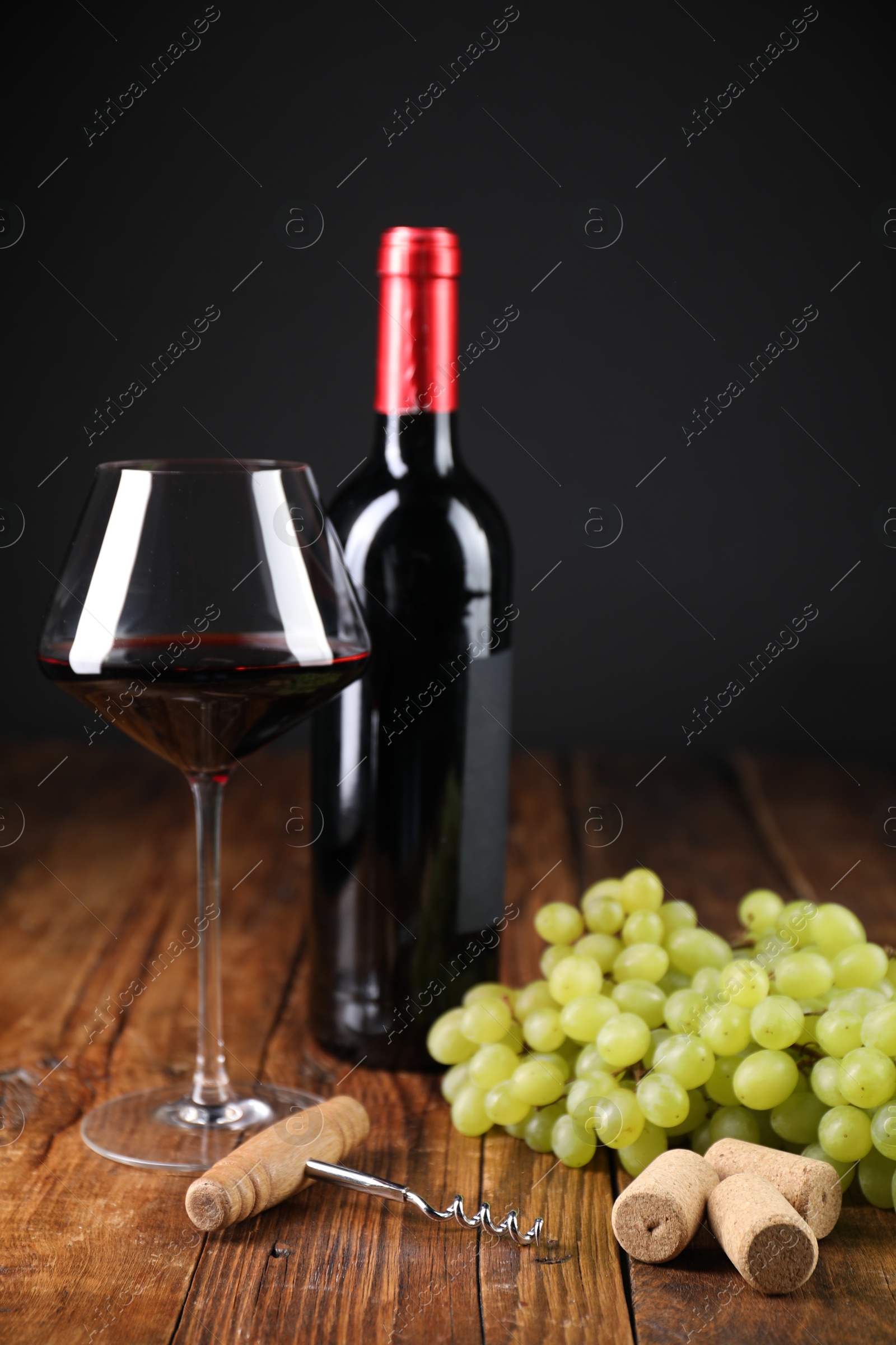 Photo of Corkscrew, corks, bottle of wine, glass and grapes on wooden table