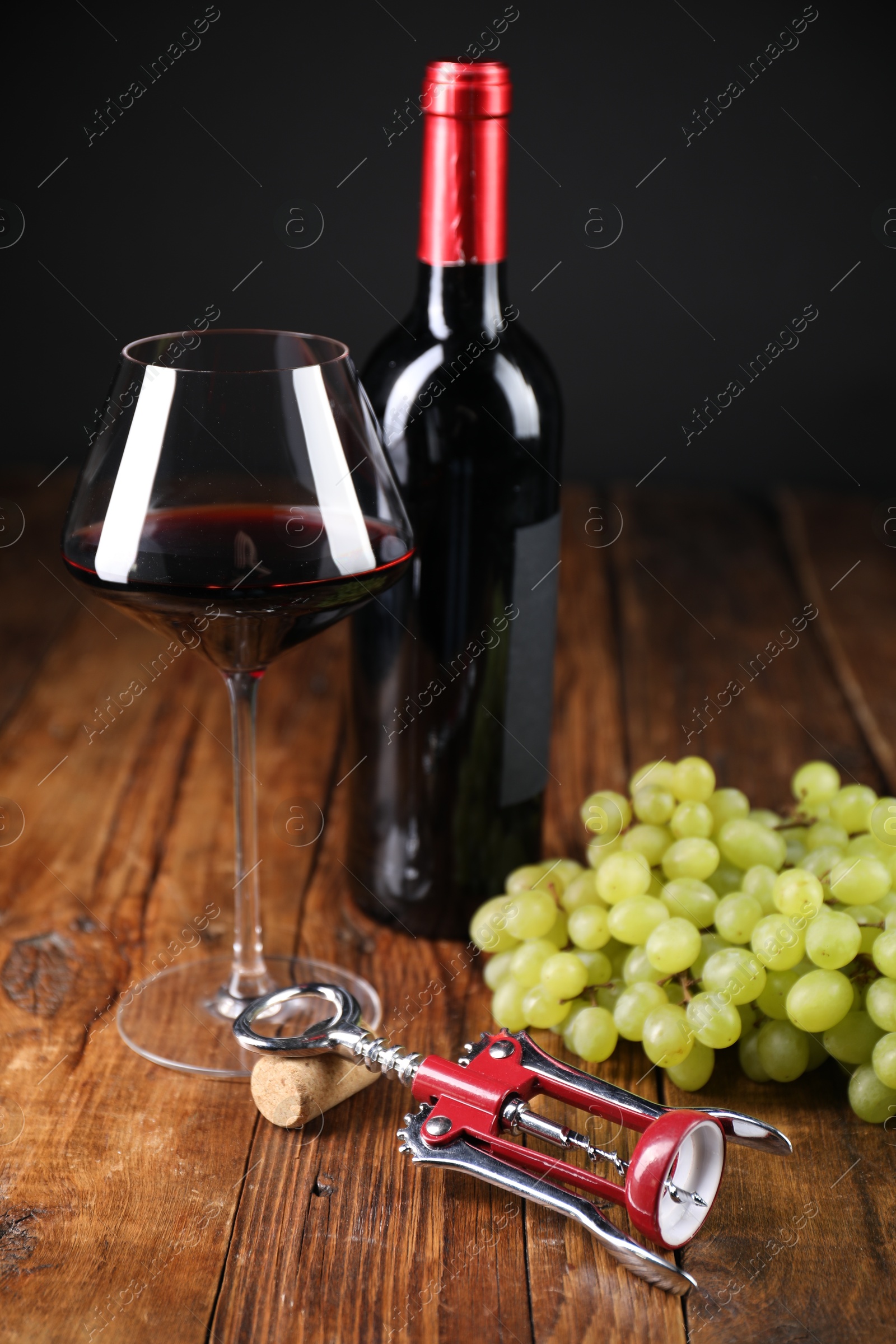 Photo of Wing corkscrew, cork, bottle of wine, glass and grapes on wooden table