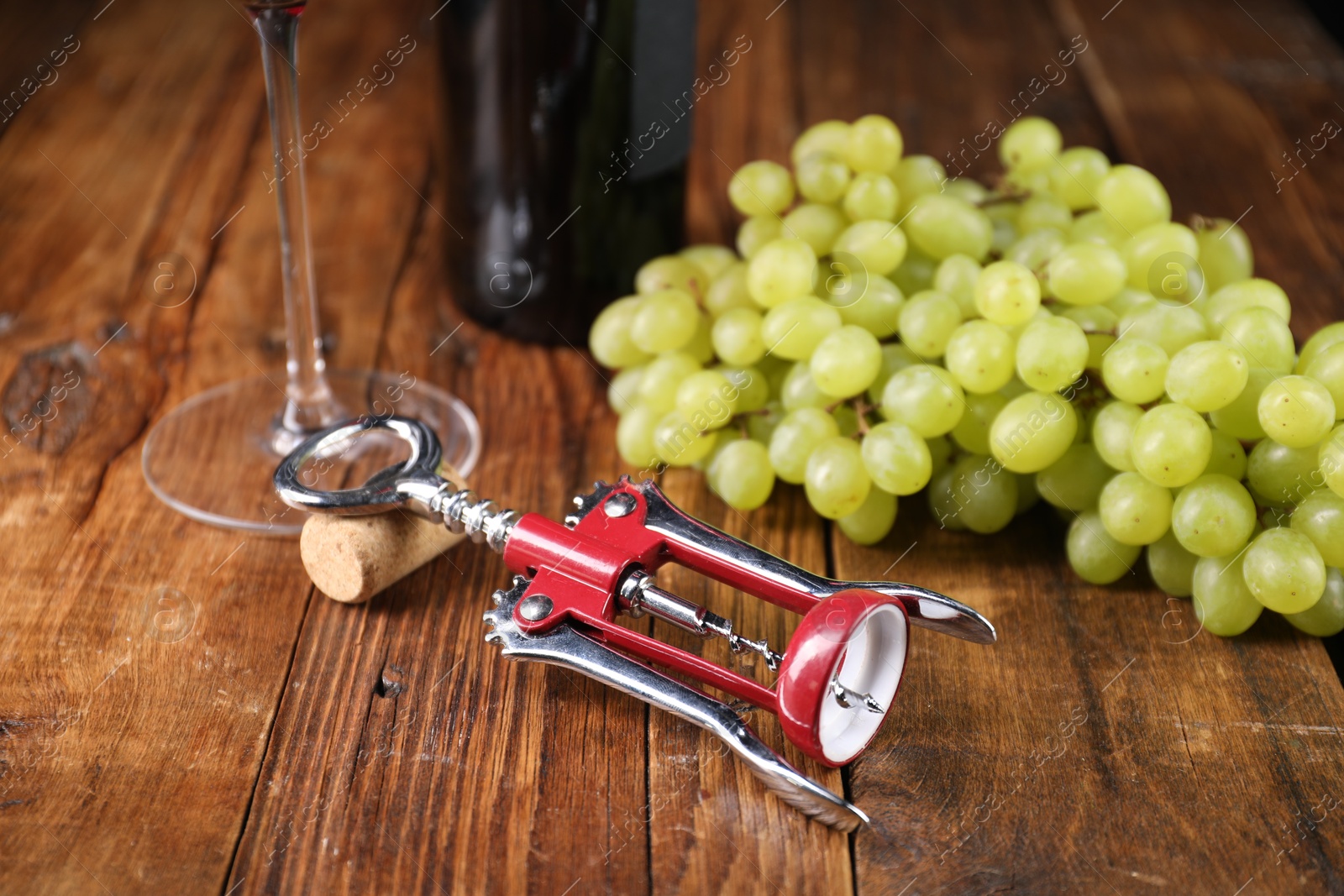 Photo of Wing corkscrew, cork and grapes on wooden table, closeup