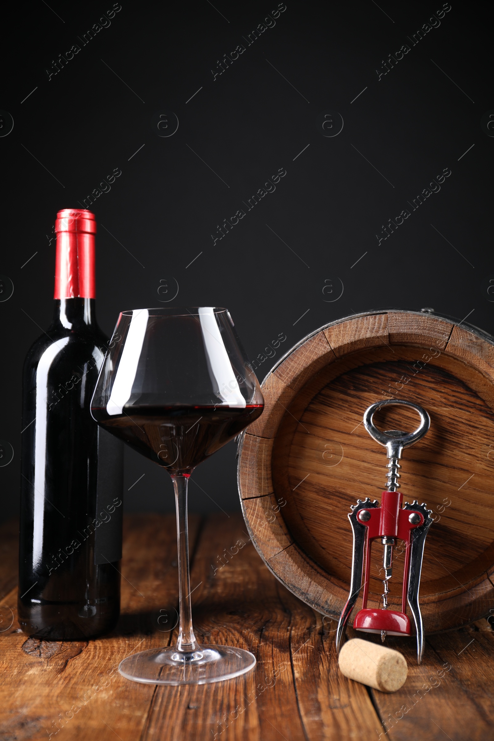 Photo of Wing corkscrew, cork, bottle of wine, glass and barrel on wooden table