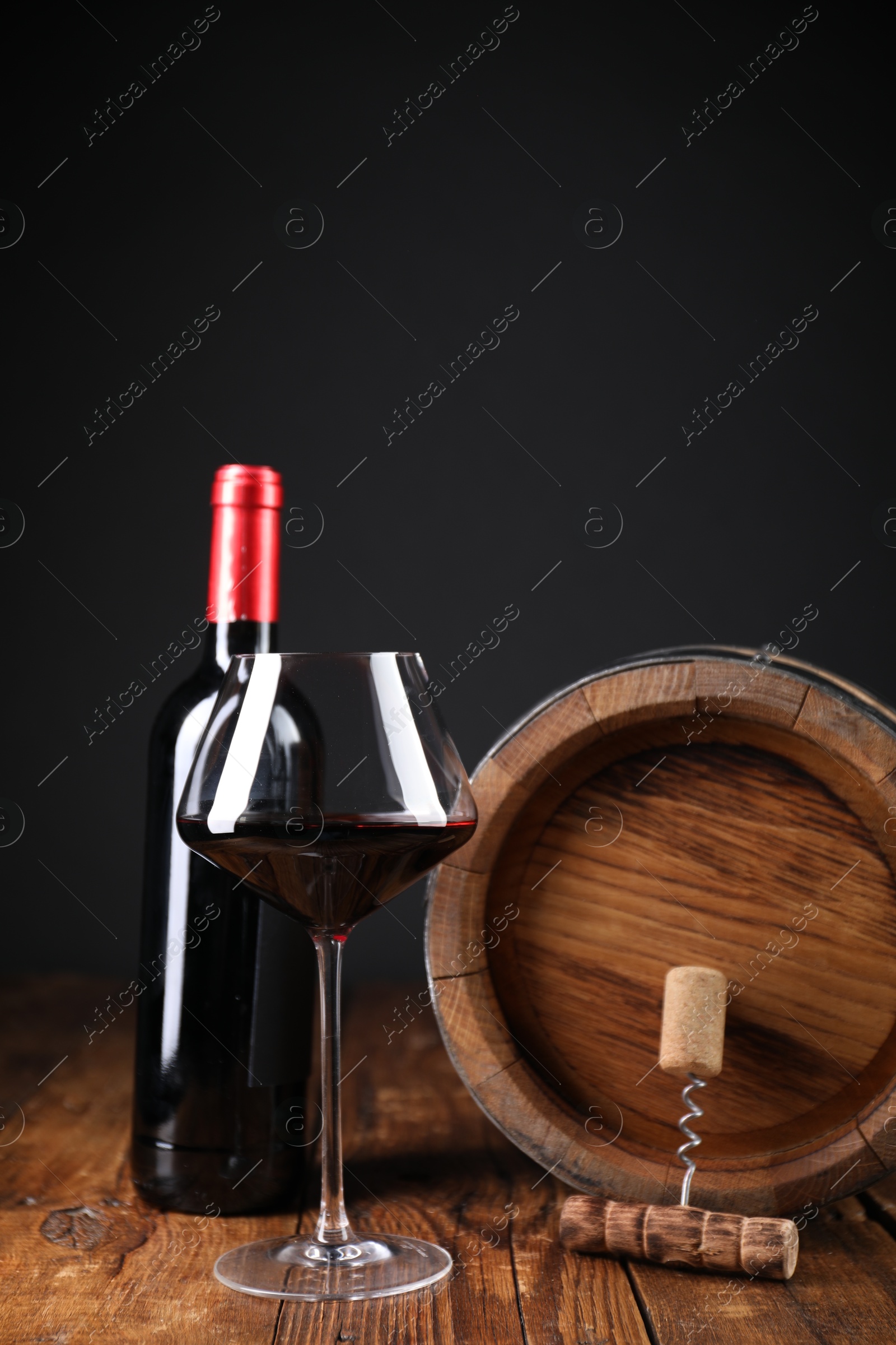 Photo of Corkscrew, cork, bottle of wine, glass and barrel on wooden table