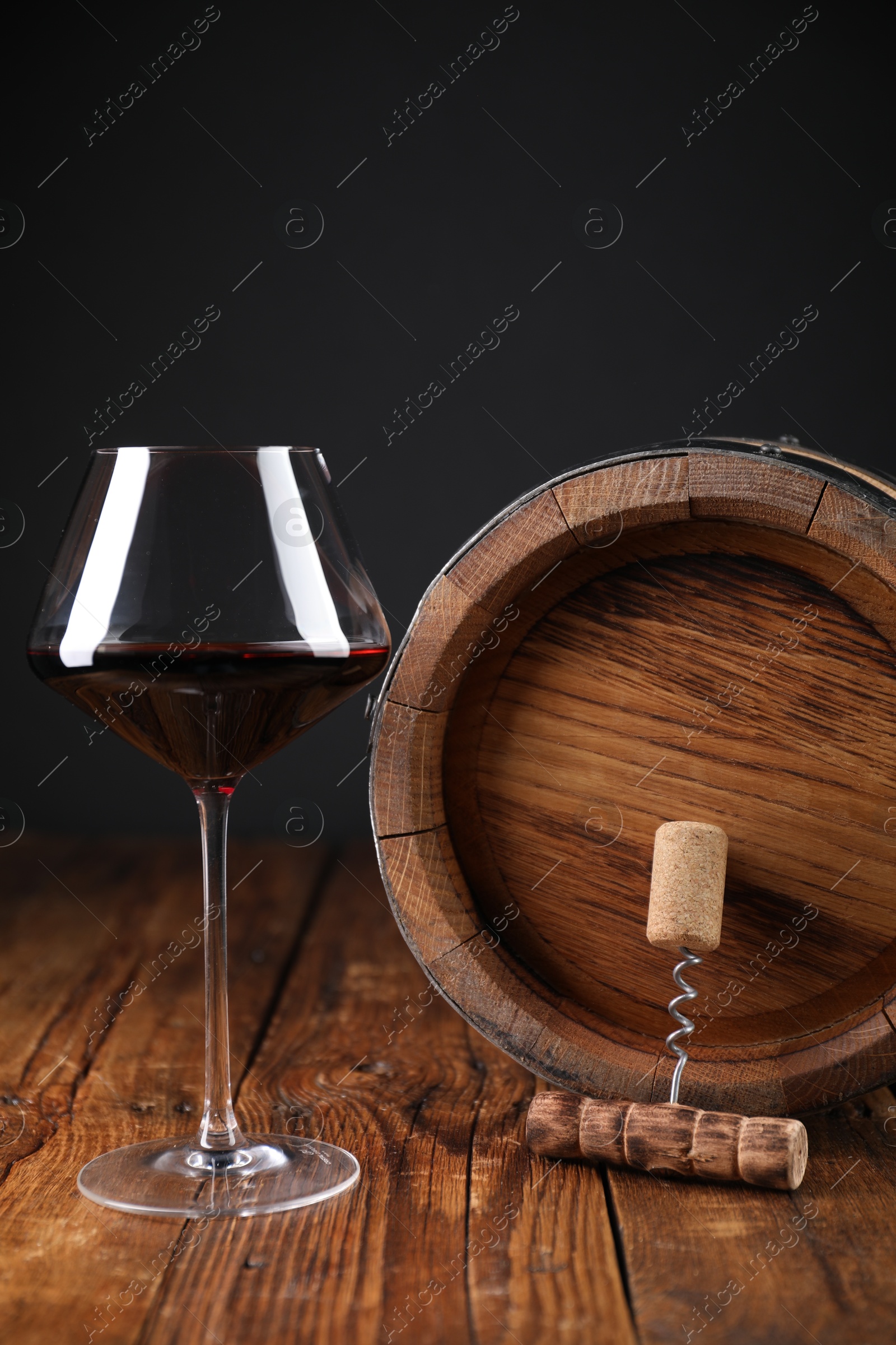 Photo of Corkscrew, cork, glass of wine and barrel on wooden table