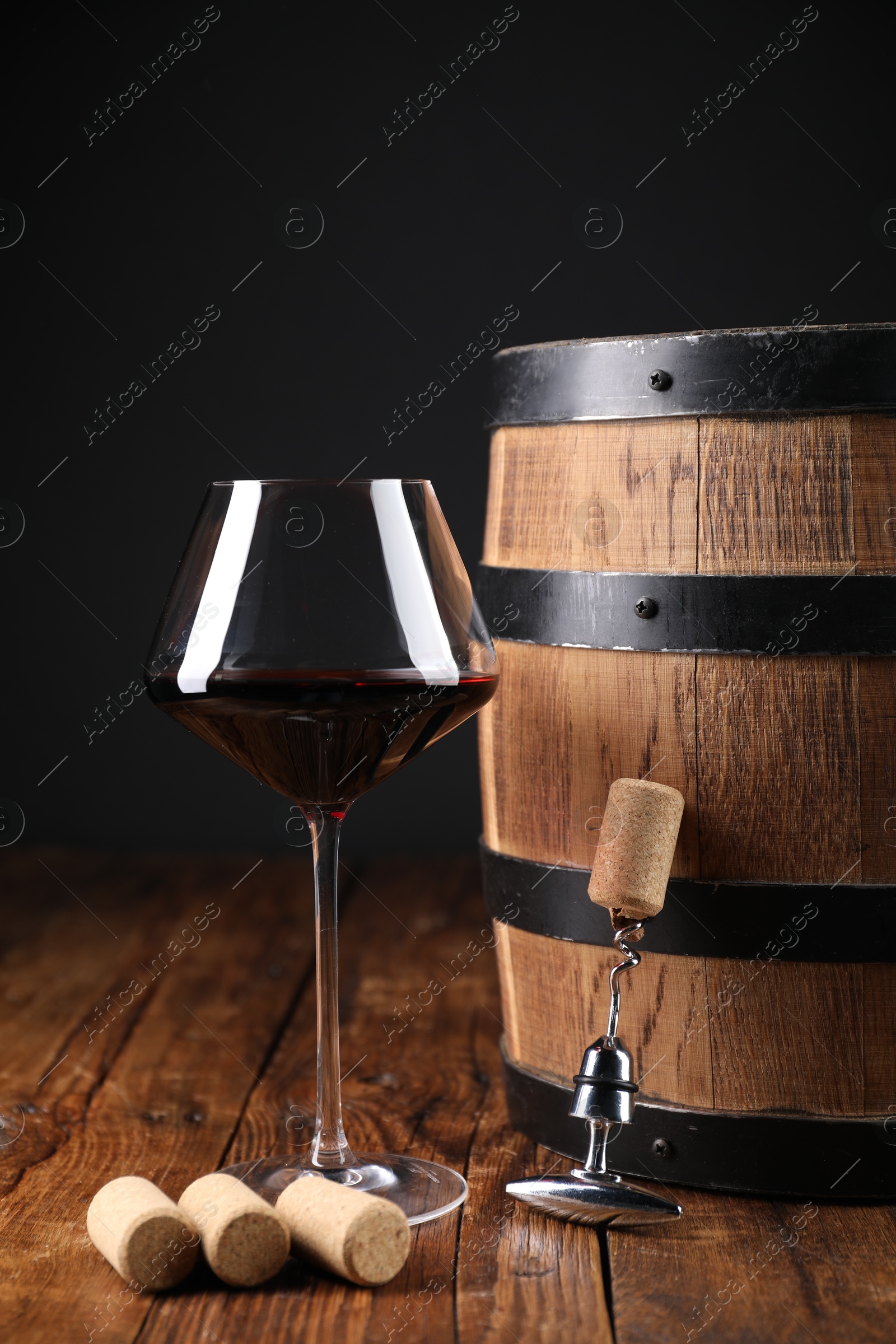 Photo of Corkscrew with metal handle, corks, glass of wine and barrel on wooden table