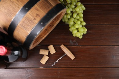 Photo of Corkscrew, grapes, corks, bottle of wine and barrel on wooden table, top view